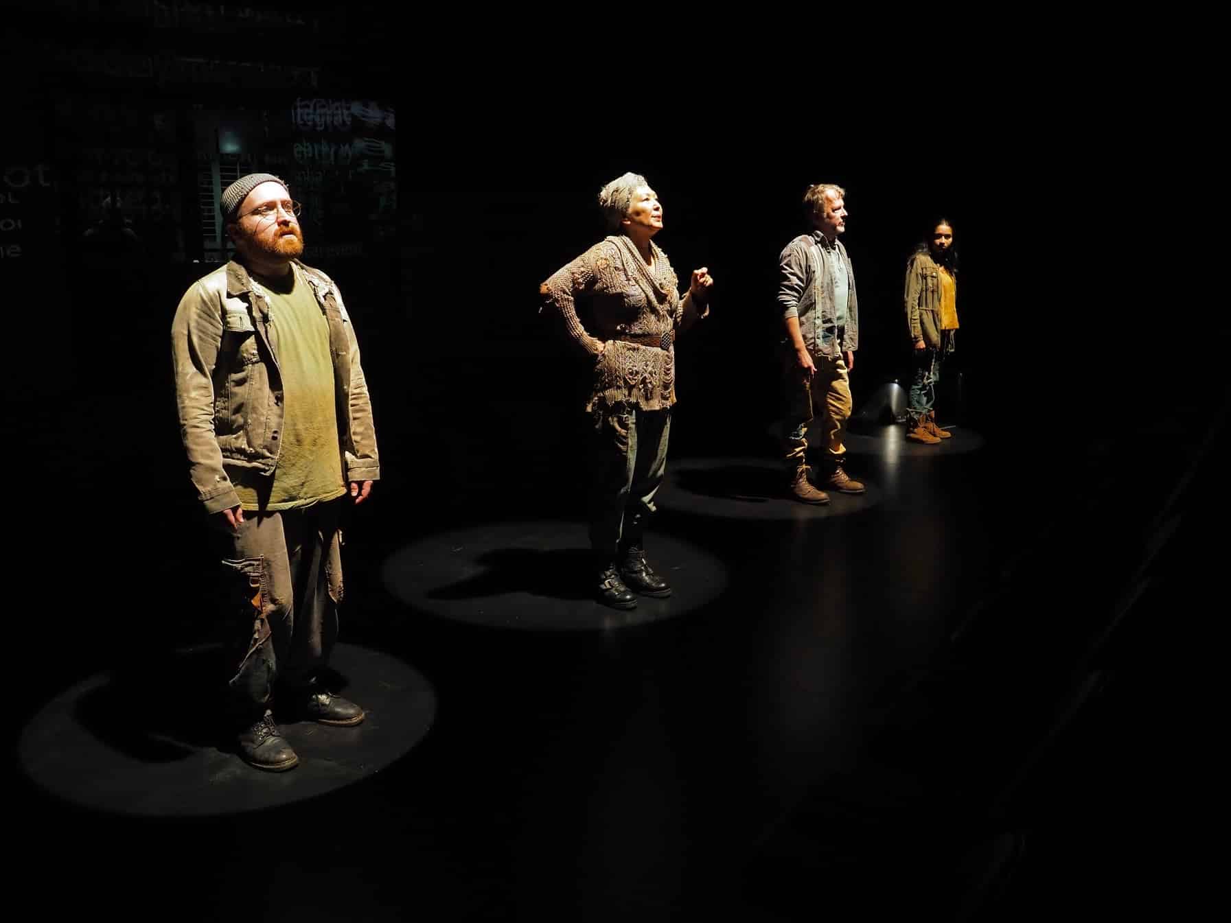 A group of people stand facing forward on a dark stage.